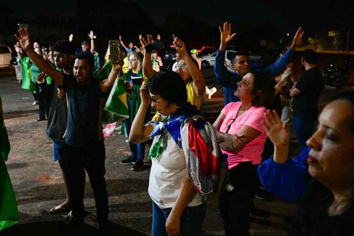 Apoiadores do ex-presidente brasileiro Jair Bolsonaro rezam em frente ao seu condomínio em Brasília, em 11 de setembro de 2025. — Foto: Pablo Porciúncula/AFP